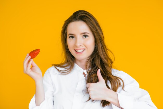 La freschezza viene in rosso Primo piano della bella donna che tiene fragola in mano