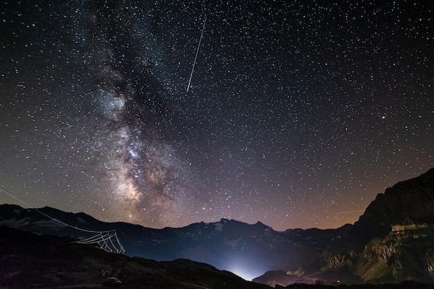 La galassia della Via Lattea e le stelle sulle Alpi francesi italiane. Cielo notturno su maestose montagne innevate e ghiacciai. Pioggia di meteoriti a destra