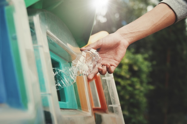 La gente che mette la bottiglia di plastica per riciclare il recipiente al parco