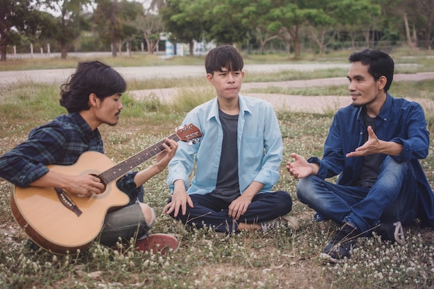 La gente del gruppo Amici asiatici dell'uomo che giocano la chitarra all'aperto