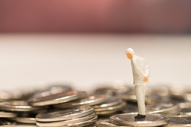 La gente in miniatura dell'uomo d'affari figura in piedi sulla pila di monete