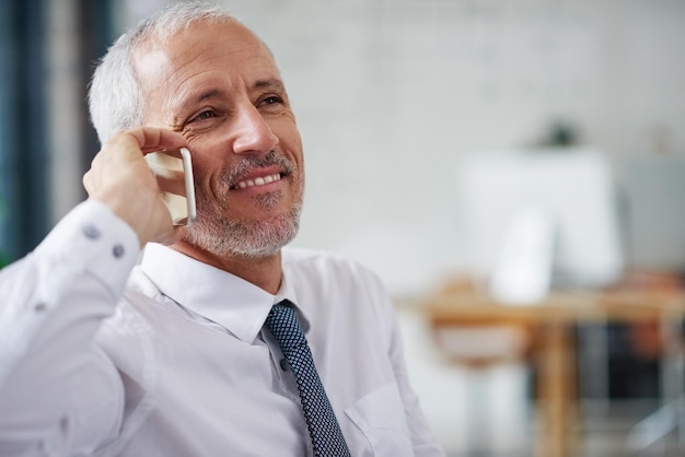 La gente lo chiama per consigli d'affari Colpo di un uomo d'affari maturo sorridente che parla su un cellulare mentre lavora in un ufficio