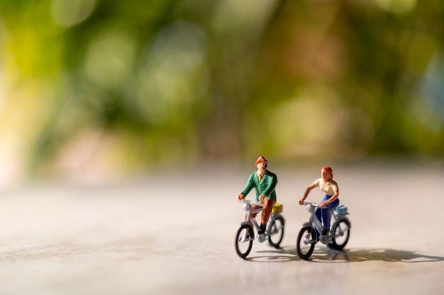 La gente miniatura guida una bicicletta all'aperto con il fondo verde del bokeh