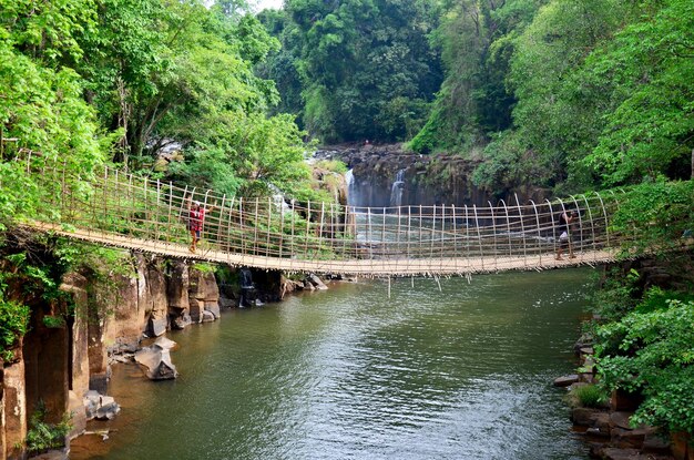 La gente tailandese e la donna viaggiano e posano la foto di scatto sul ponte sospeso di legno e di bambù per attraversare il fiume del flusso alle cascate di Tad Pha Suam a Pakse Champasak Laos