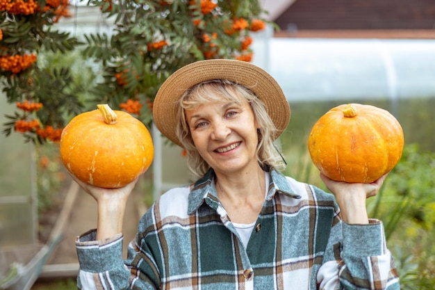 La giardiniera donna in una camicia a quadri tiene le zucche nel suo giardino Grande concetto di raccolto