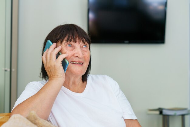La gioiosa donna caucasica in pensione in abiti casual si sta rilassando a casa con una piacevole conversazione telefonica...