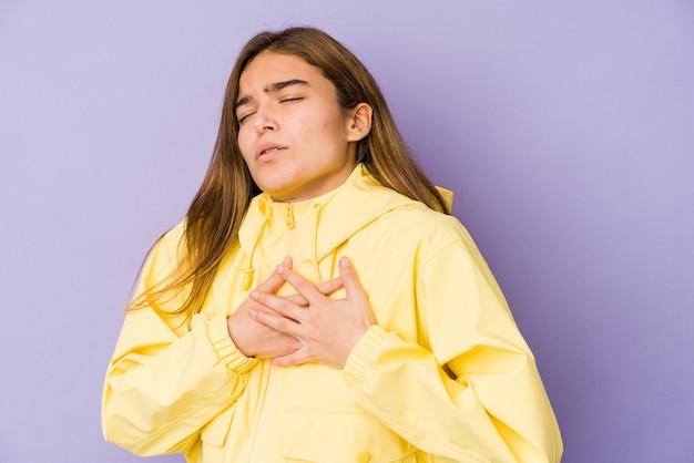 La giovane adolescente magra della ragazza caucasica su sfondo viola ha un'espressione amichevole, premendo il palmo sul petto. Concetto di amore.