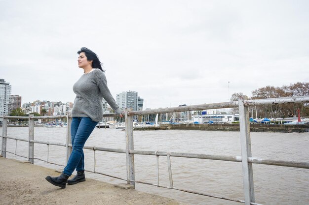 la giovane avventurosa turista latina è in piedi appoggiata alla ringhiera del molo sul fiume