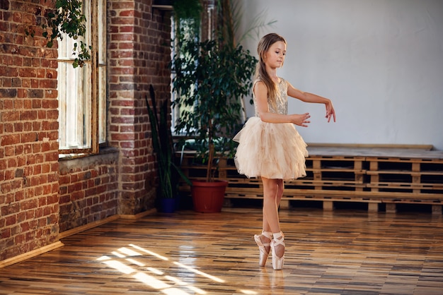 La giovane ballerina in tutu e scarpe da punta che praticano la danza si muove nella sala da ballo.