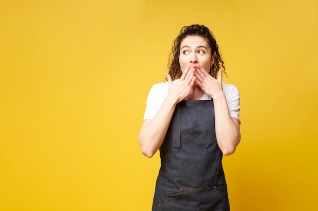 La giovane barista scioccata in uniforme si copre la bocca con le mani e mostra sorpresa