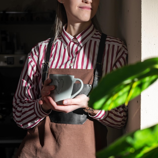 La giovane barista vicino a una finestra moderna si gode una tazza di caffè guardando fuori buongiorno giorno lavorativo libero dal lavoro e dai doveri