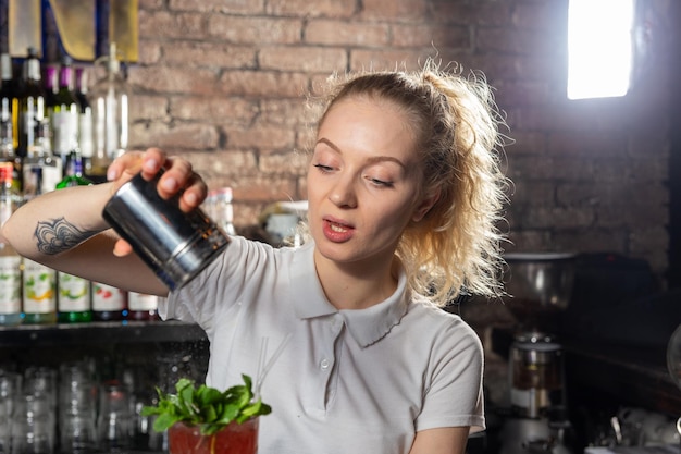 La giovane bella barista femminile cosparge il cocktail di zucchero a velo