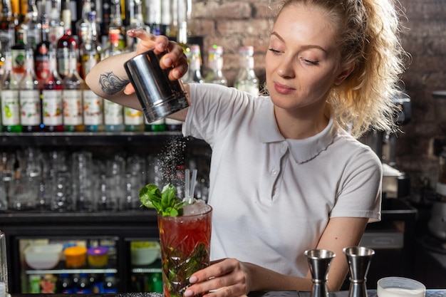 La giovane bella barista femminile cosparge il cocktail di zucchero a velo