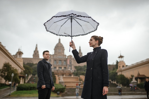 La giovane bella coppia ispanica amorosa cammina sotto un ombrello durante la pioggia in plaza Spagna. Coppia in posa sullo sfondo del Museo Nazionale d'Arte della Catalogna.