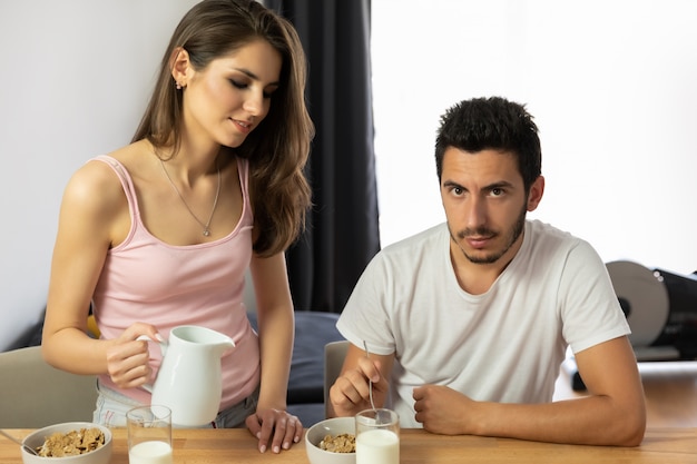 La giovane bella coppia mangia il cereale da prima colazione con le bacche e il latte.