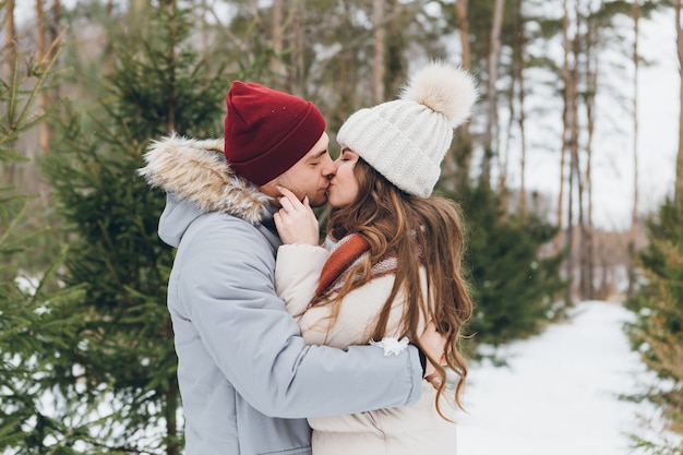 La giovane bella coppia si abbraccia in una foresta di conifere d'inverno