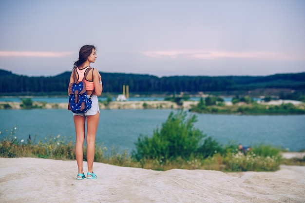 La giovane bella donna abbronzata viaggia con uno zaino. Camminando vicino ai laghi.