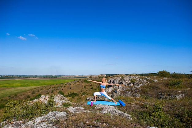 La giovane bella donna bionda che fa l&#39;yoga si esercita su una roccia. Handstand. Palestra fitness e sport all&#39;aria aperta