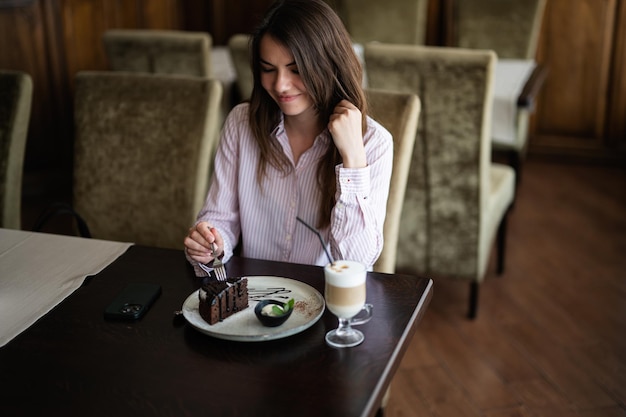 La giovane bella donna castana si siede nel ristorante del caffè della caffetteria all'interno