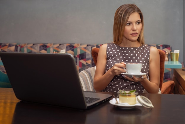 La giovane bella donna castana sorridente lavora sul computer portatile in caffè