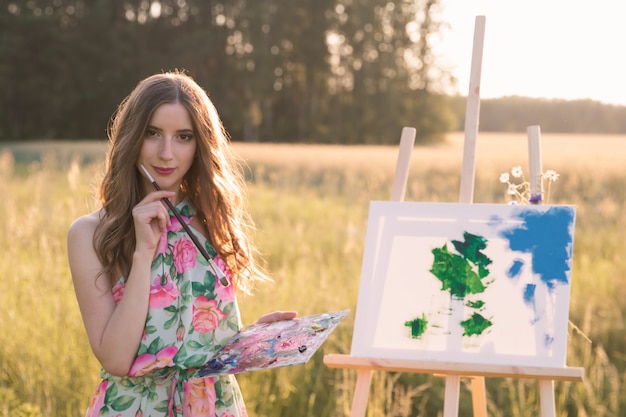 La giovane bella donna con capelli naturali lunghi disegna una pittura all'aperto