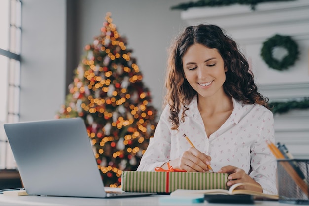 La giovane bella donna d'affari italiana felice firma preparata una confezione regalo di Natale per il cliente in ufficio