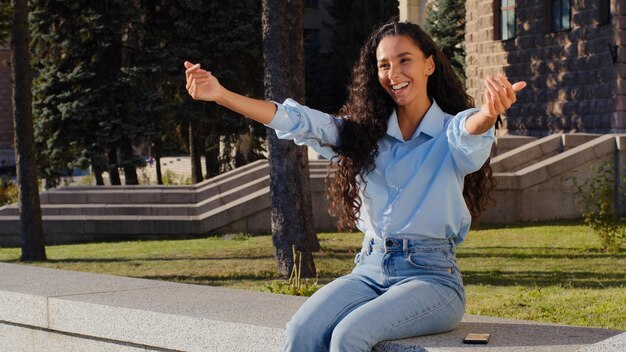 La giovane bella donna della ragazza che sorride nell'invito di gesto di saluto della via della città viene su benvenuto