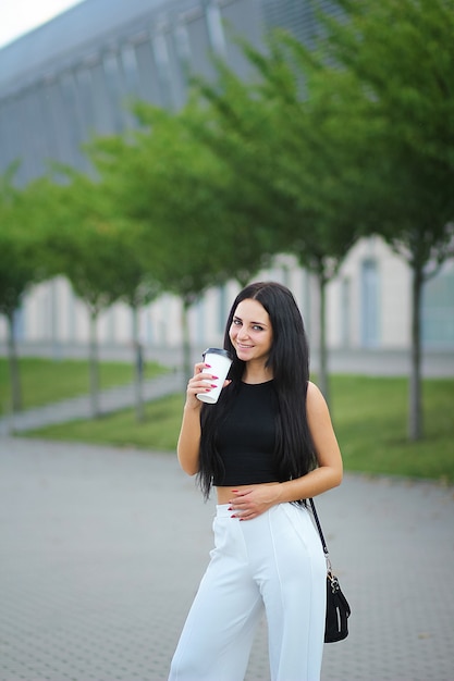 La giovane bella donna di affari beve il caffè vicino accanto all'edificio per uffici