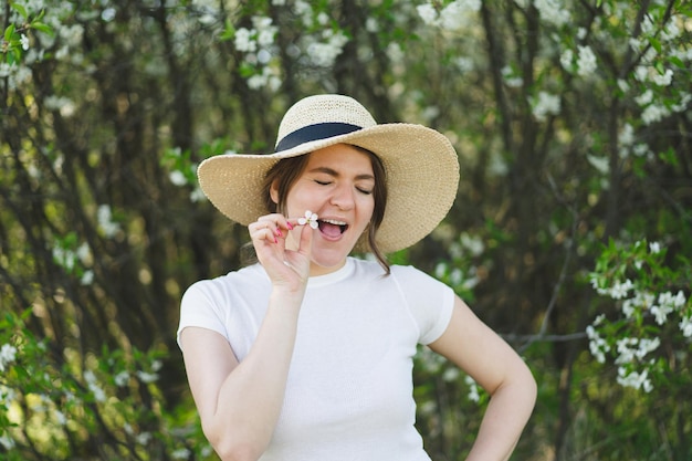 La giovane bella donna divertente con un cappello tra gli alberi in fiore respira la donna felice libera nessuna allergia