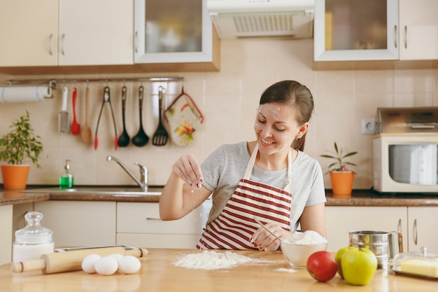 La giovane bella donna felice seduta a un tavolo con la farina e andando a preparare una torta in cucina. Cucinare a casa. Prepara da mangiare.