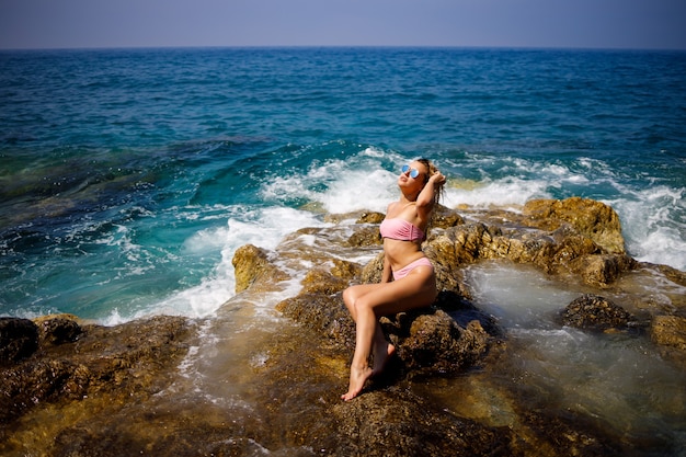 La giovane bella donna in costume da bagno si siede su una spiaggia rocciosa del Mar Mediterraneo in Turchia. Il concetto di ricreazione del mare. Messa a fuoco selettiva