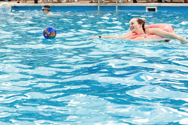 la giovane bella donna in un cerchio gonfiabile nuota e gioca a giochi attivi con una palla in piscina