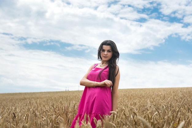 La giovane bella donna in un vestito cammina su un'estate dorata del campo di grano
