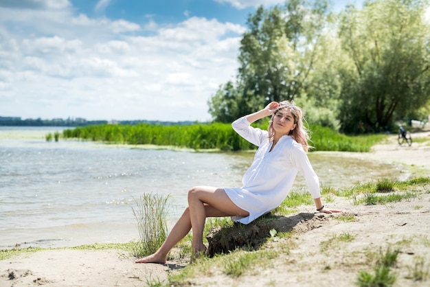 La giovane bella donna in vestito bianco gode della natura vicino al lago, libertà. giorno d'estate