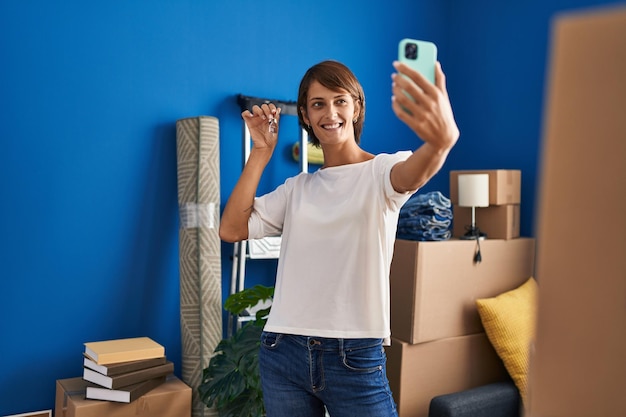 La giovane bella donna ispanica fa il selfie dallo smartphone tenendo la chiave nella nuova casa