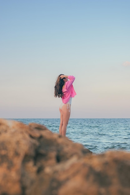 La giovane bella donna posa con il mare sullo sfondo al tramonto