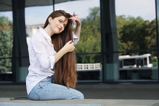 La giovane bella donna sorridente raddrizza i suoi capelli lunghi