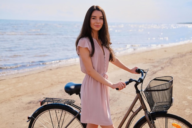 La giovane bella donna sta godendo l'estate con la sua bicicletta al mare nella luminosa giornata di sole.