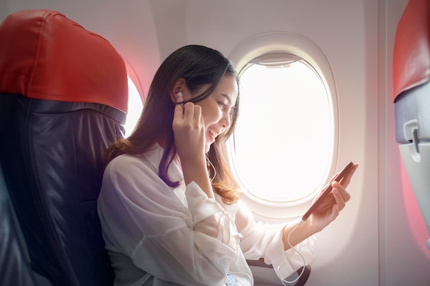 La giovane bella donna sta usando lo smartphone sul concetto di viaggio e vacanze in aereo