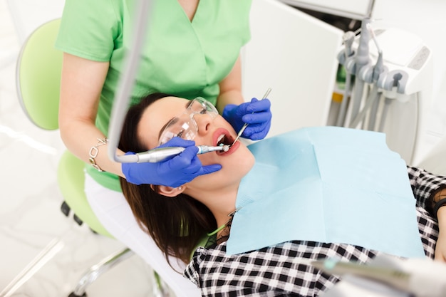 La giovane bella donna tratta i denti al gabinetto del dentista. Processo di trattamento dentale