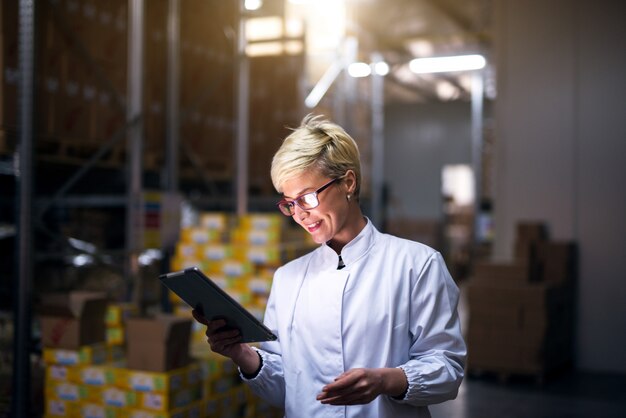 La giovane bella lavoratrice allegra è soddisfatta della quota giornaliera raggiunta che ha visto sul tablet mentre si trovava nell'hangar di stoccaggio.