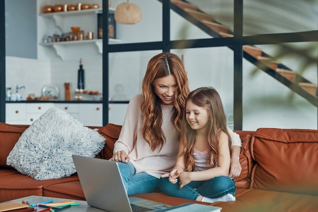 La giovane bella madre e la sua piccola figlia si uniscono e sorridono mentre usano il laptop a casa