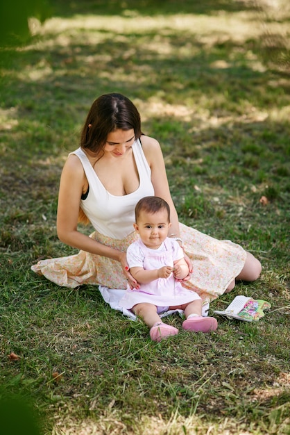 La giovane bella madre si siede con il suo bambino sull'erba in un parco.