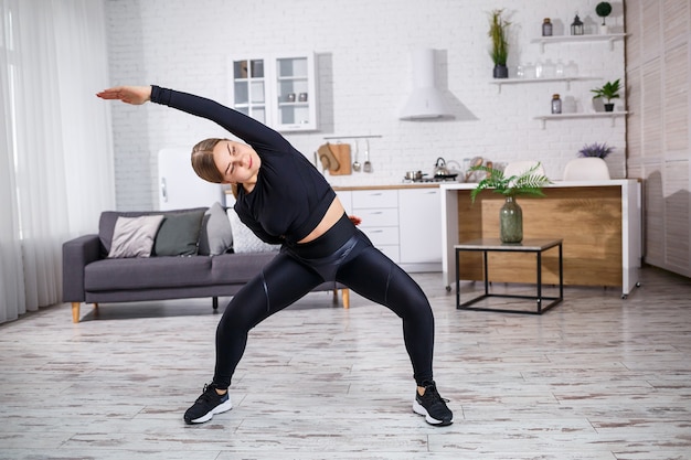 La giovane bella ragazza atletica in leggings e un top fa esercizi di stretching. Uno stile di vita sano. La donna fa sport a casa.