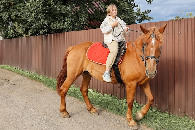 La giovane bella ragazza cavalca il suo cavallo per le strade di campagna in autunno