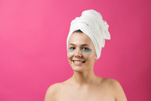 La giovane bella ragazza con un asciugamano bianco sulla testa indossa cerotti in gel di collagene sotto gli occhi. Maschera sotto gli occhi trattamento viso.