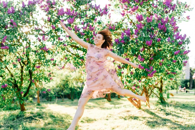 La giovane bella ragazza di modello alla moda in vestito si diverte all'aperto nel giardino di fioritura lilla nel giorno di estate.