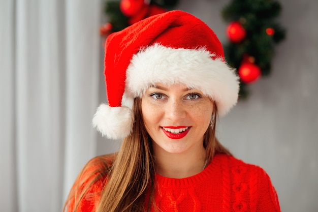 La giovane bella ragazza in cappello di natale esamina la macchina fotografica