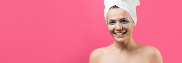La giovane bella ragazza in un asciugamano bianco sulla testa indossa cerotti in gel di collagene sotto gli occhi Maschera sotto il viso per il trattamento degli occhi