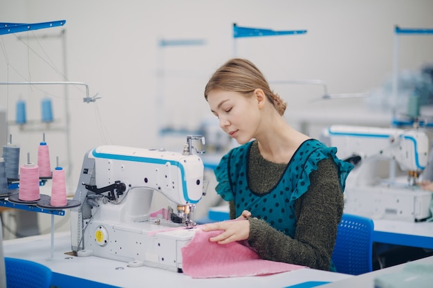 La giovane bella sarta cuce sulla macchina da cucire in fabbrica.